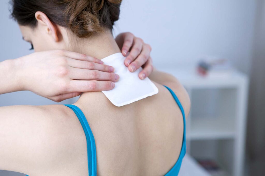 lady putting cold pad on her upper back at base of neck